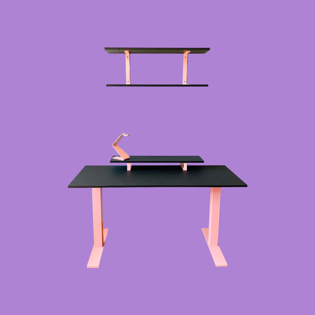 Matte black desk with a pink desk frame, a matte black monitor riser with pink feet and a pink headphone stand, and a matte black wall shelf with pink brackets.