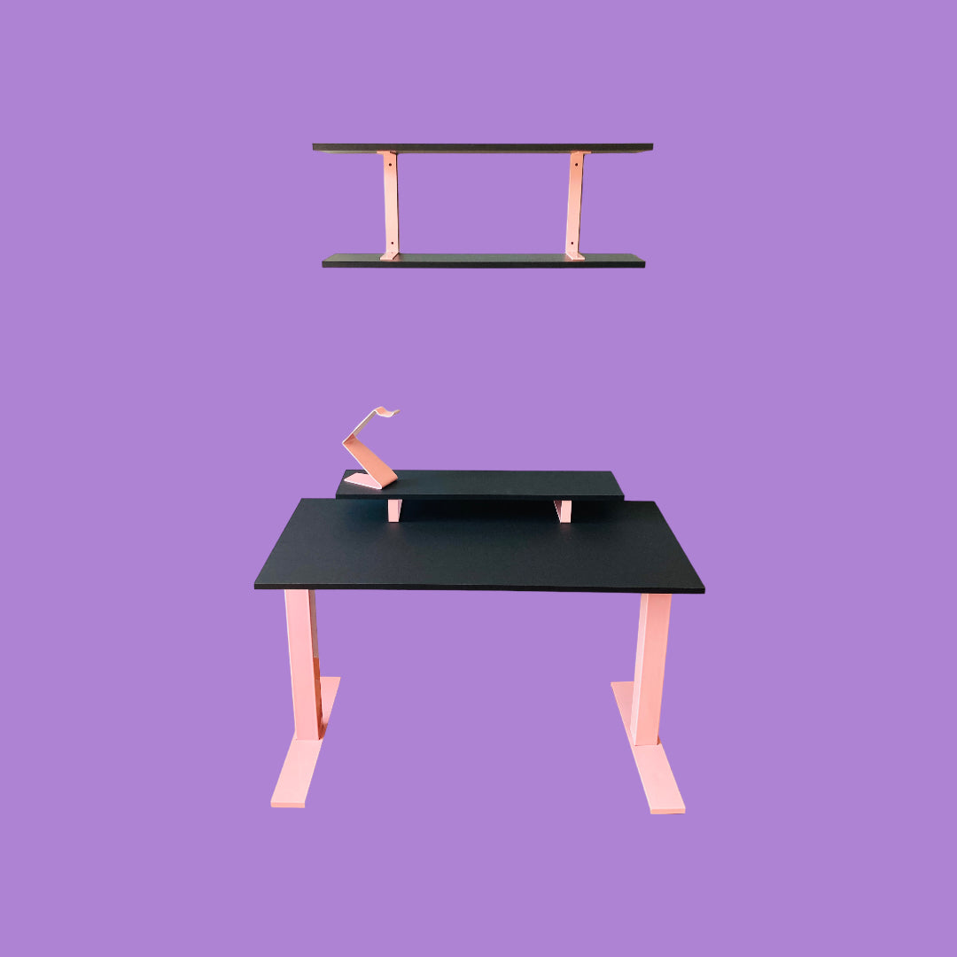 Matte black desk with a pink desk frame, a matte black monitor riser with pink feet and a pink headphone stand, and a matte black wall shelf with pink brackets.